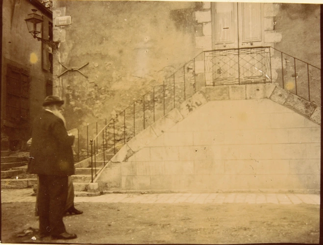 Anonyme - Auguste Delaherche debout, de dos, devant les marches d'une maison