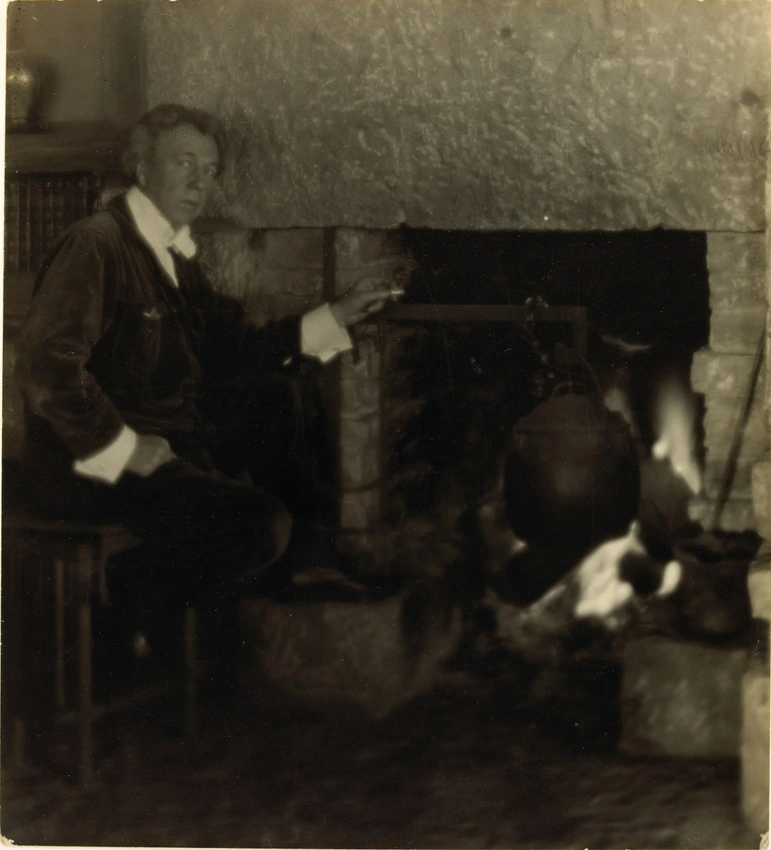 Anonyme - Frank Lloyd Wright assis sur une petite table, près de la cheminée, da...