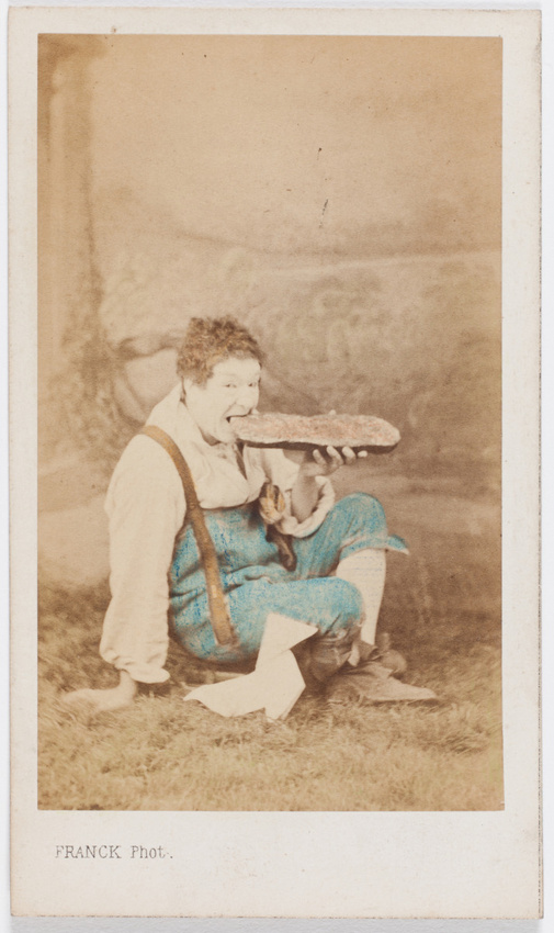 Franck - Paul Legrand en habit de scène (paysan), assis les jambes croisées, dév...