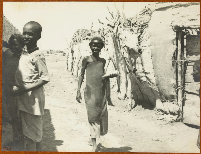 Trois enfants sur un chemin entre un mur et des huttes - Anonyme