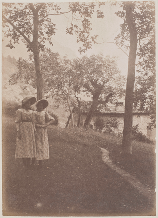 Yvonne et Christine Lerolle, en robes à fleurs et chapeau, debout dans un jardin arboré - Anonyme