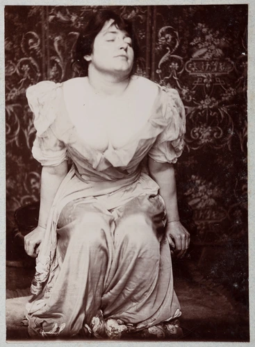 Anonyme - Lili Grenier assise, portant une robe blanche et penchée en avant