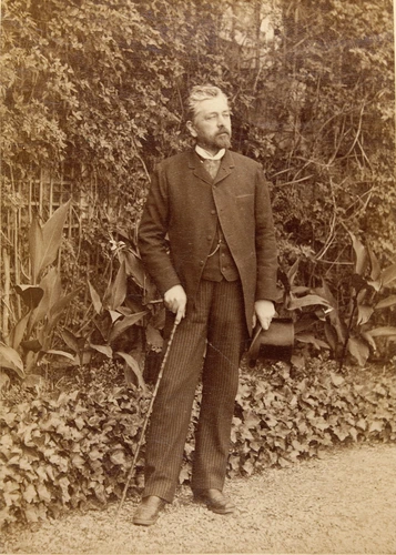 Gustave Eiffel dans un jardin, debout, en pied canne et chapeau en main - Anonyme