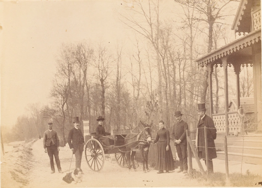 Groupe de six personnes dont une est dans une voiture tirée par un âne devant l'entrée d'un chalet, dans un bois - Gustave Eiffel