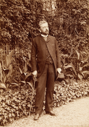 Anonyme - Gustave Eiffel dans un jardin, debout, en pied canne et chapeau en mai...
