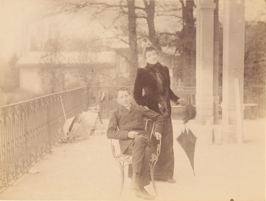 Jeune femme debout à côté d'un jeune garçon assis sur un siège en métal, sur la terrasse du Clos des Bruyères - Gustave Eiffel