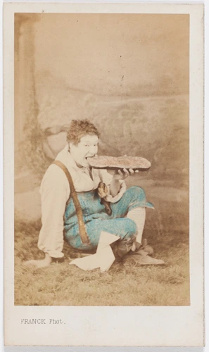 Paul Legrand en habit de scène (paysan), assis les jambes croisées, dévorant une tartine de pain, une cocotte en papier contre la jambe - Franck